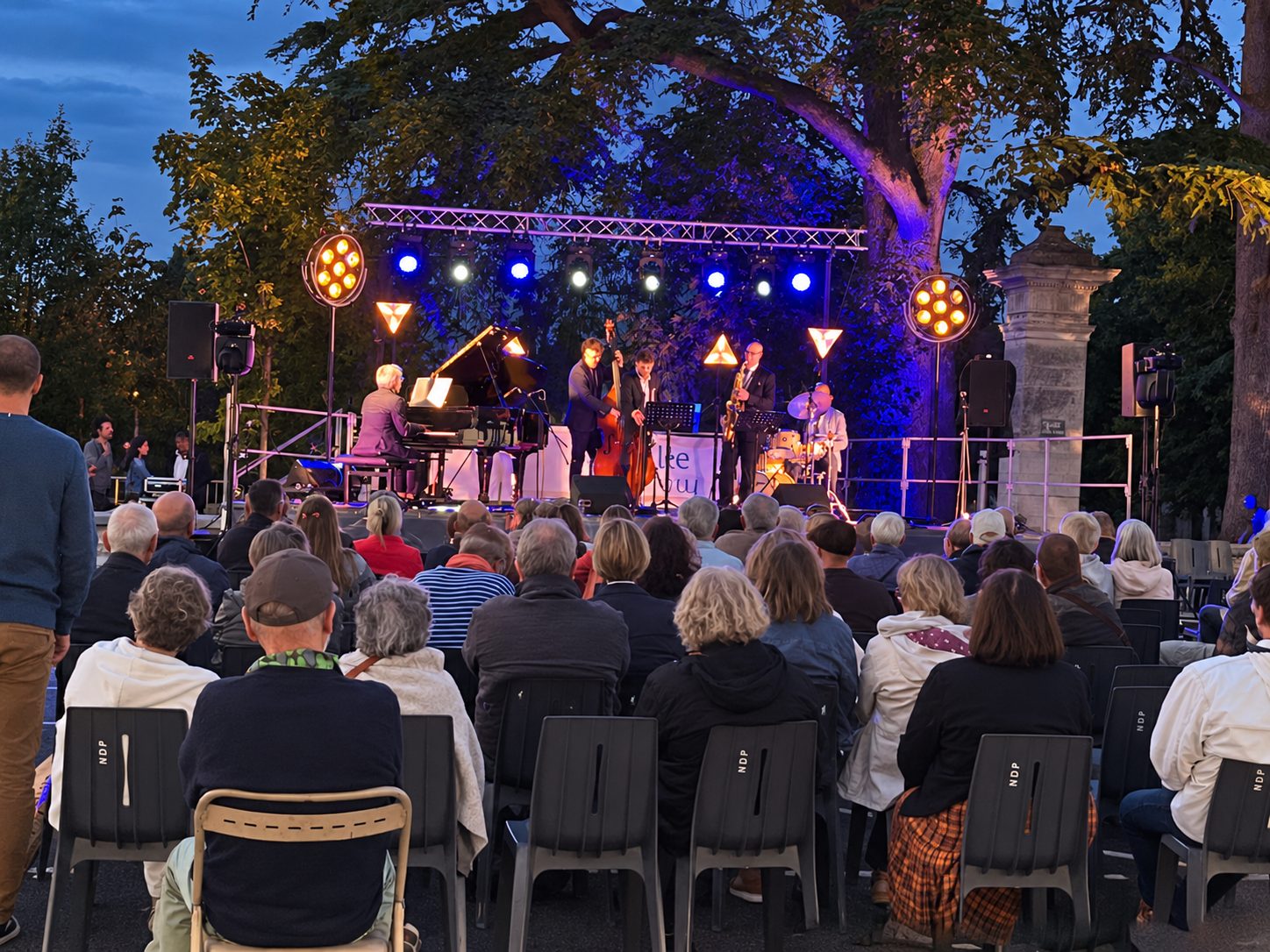 Public réuni devant une scène de concert éclairée en extérieur