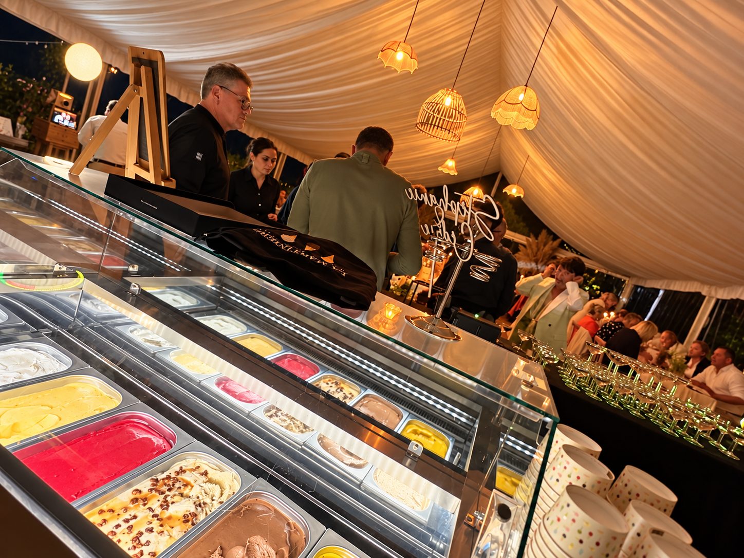 Vue du comptoir de glaces et des invités sous les luminaires de la tente