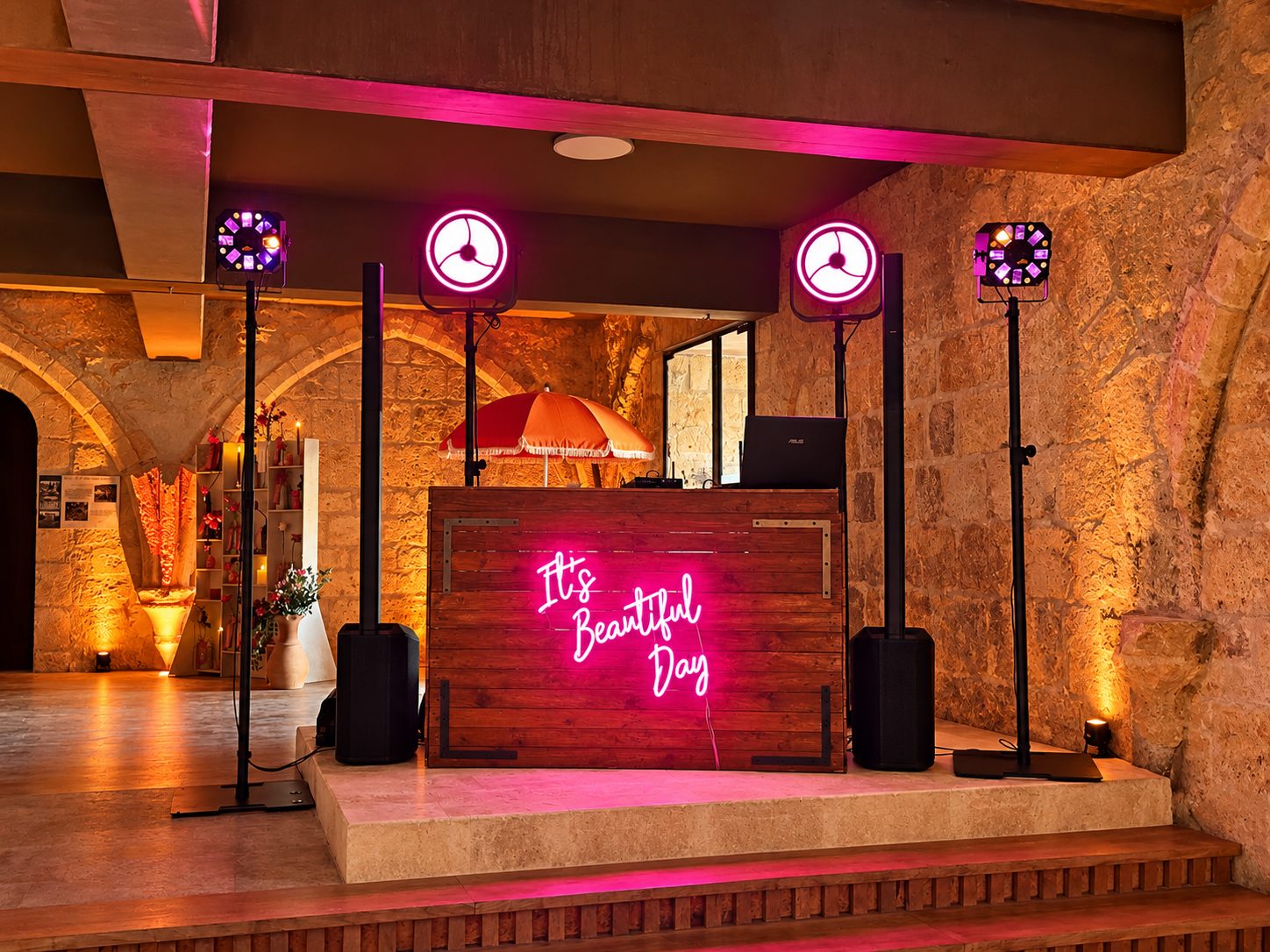 Bar DJ en bois sur une estrade, avec enseigne lumineuse rose et éclairage de piste