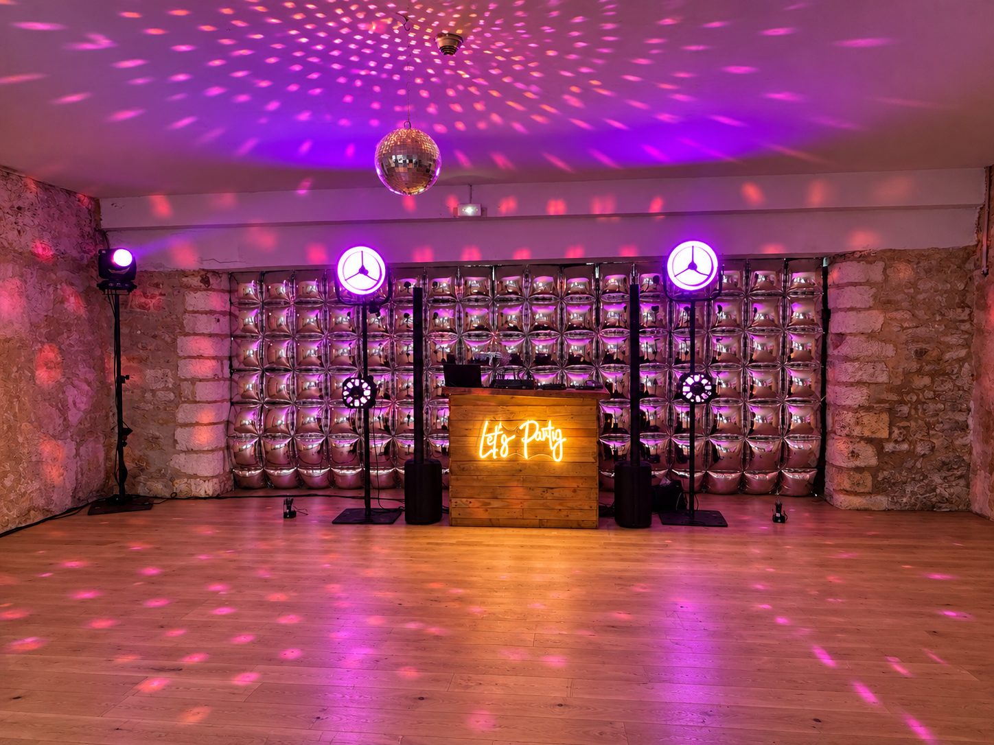Bar DJ en bois, boule à facettes et effets lumineux roses sur la piste de danse
